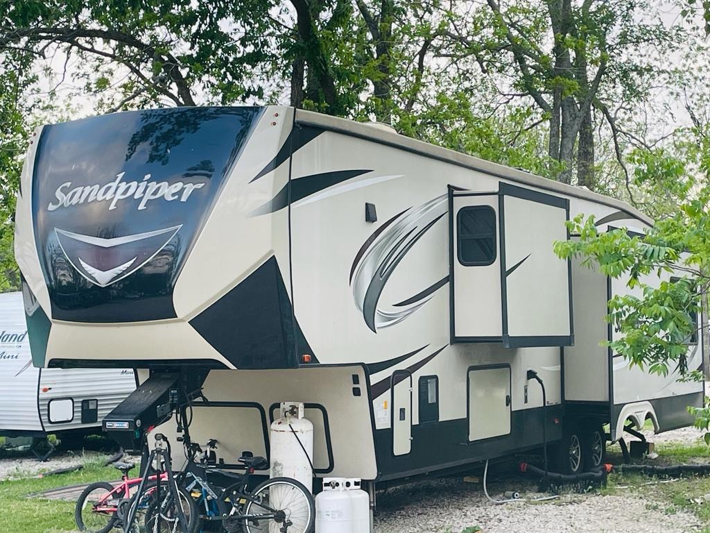 Forest River Sandpiper fifth-wheel RV with bicycles parked under trees at Sugar Land RV Park
